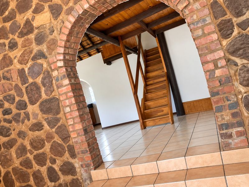Spacious living area featuring a rustic stone feature wall, brick archway, tiled floors, and a prominent wooden staircase leading to an upper level.