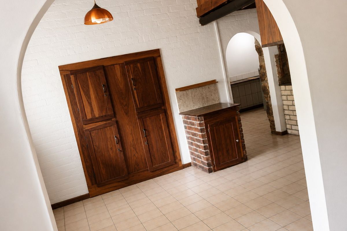 A rustic kitchen area featuring built-in wooden cabinetry, brick-based counter, tiled flooring, and distinctive arched architectural details.