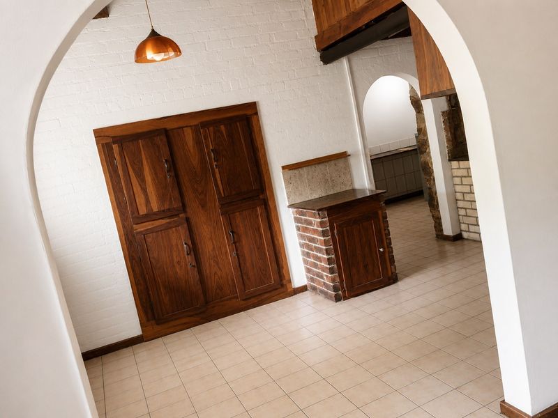 A rustic kitchen area featuring built-in wooden cabinetry, brick-based counter, tiled flooring, and distinctive arched architectural details.