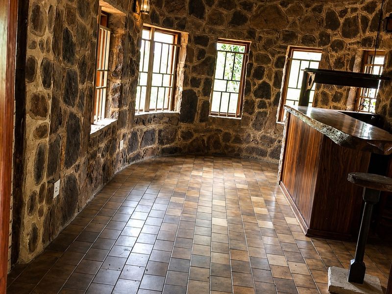 A rustic bar area featuring stone walls, a traditional thatched roof, ceramic tile flooring, and a built-in wooden bar counter.