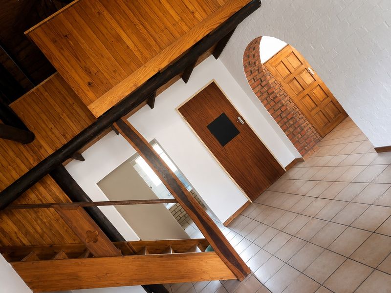A spacious hallway featuring a wooden staircase, exposed timber beams, tiled flooring, and a distinctive brick archway leading to an interior room.