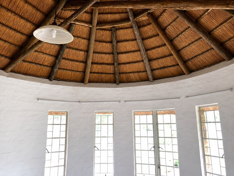 A bright, circular living space featuring a traditional thatched roof with exposed timber rafters and multiple lattice windows providing natural light.