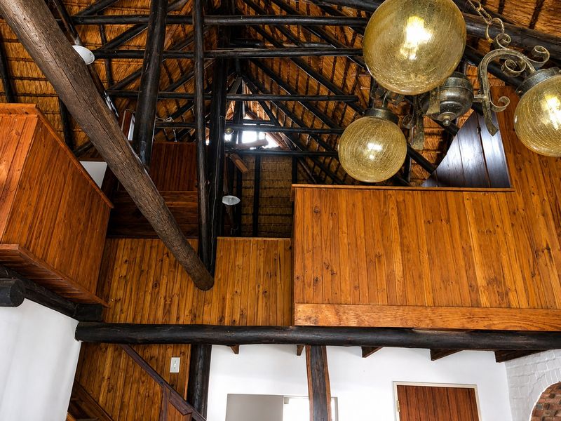 Spacious living area featuring a high-volume thatched roof with exposed timber rafters, wooden wall paneling, and a mezzanine level with a timber balustrade.