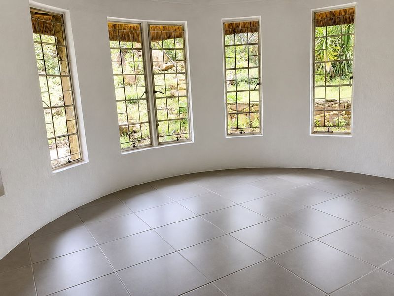 A bright, empty circular living space featuring large steel-framed windows and modern neutral floor tiles, offering a unique architectural layout.