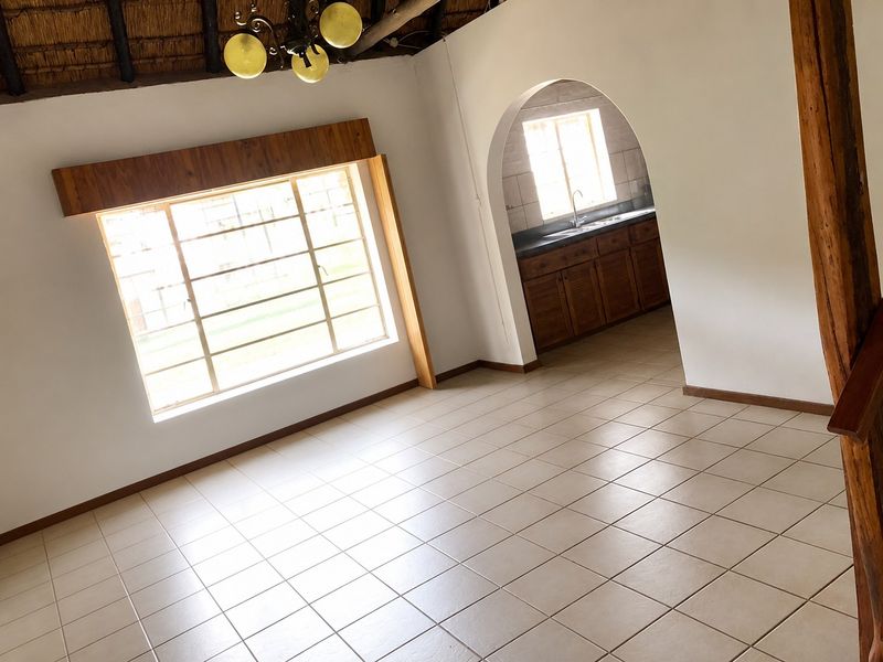 Spacious open-plan living area featuring tiled floors, a unique thatched ceiling, and an arched entryway leading into a functional kitchen space.