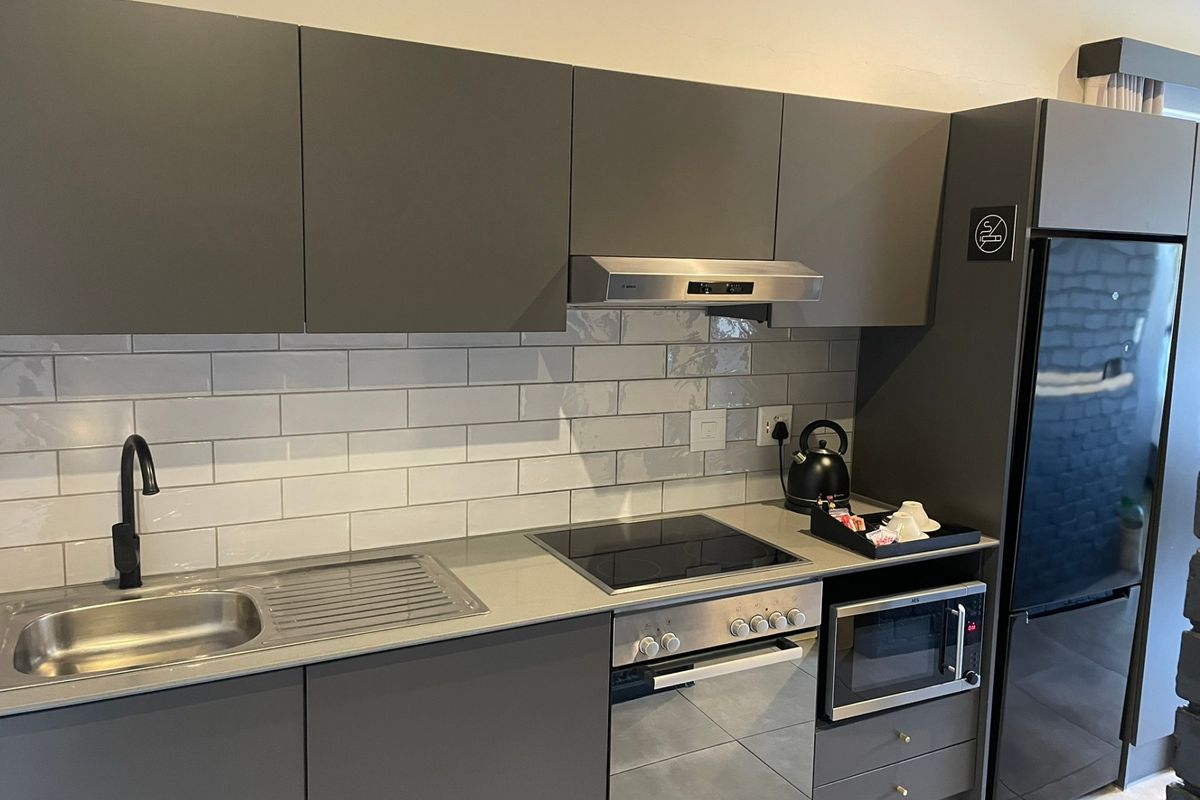 Modern kitchen featuring sleek grey cabinetry, subway tile backsplash, integrated appliances including an oven, hob, and extractor fan, and a contemporary sink.