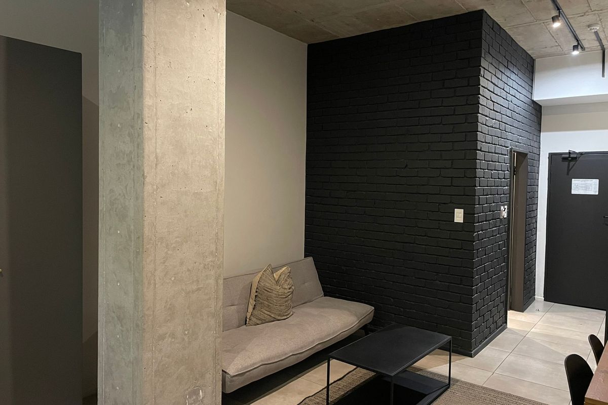 Modern living area featuring an exposed concrete ceiling, a striking black painted brick feature wall, and industrial-style concrete column detailing.