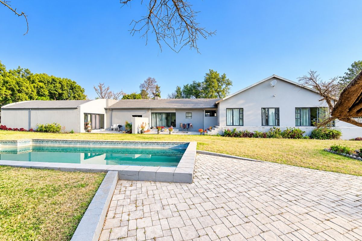 Rear view of the property featuring a swimming pool, paved patio area, and a spacious lawn set against the main house structure.