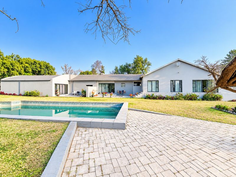 Rear view of the property featuring a swimming pool, paved patio area, and a spacious lawn set against the main house structure.