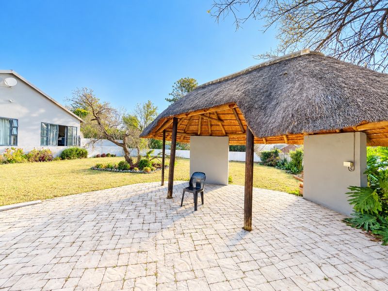 Outdoor entertainment area featuring a thatched lapa structure with paved flooring, set within a spacious garden.
