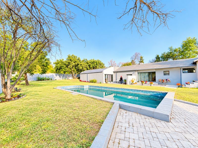A spacious backyard featuring a rectangular swimming pool, paved patio area, and well-maintained lawn, providing an ideal space for outdoor relaxation and entertainment.