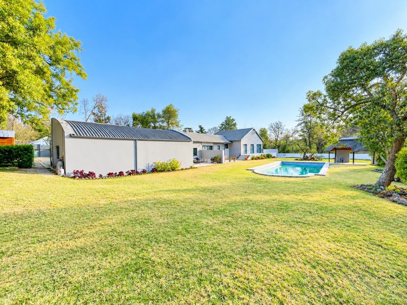 Spacious rear garden featuring a swimming pool, a detached structure with a curved metal roof, and a traditional thatched lapa area.