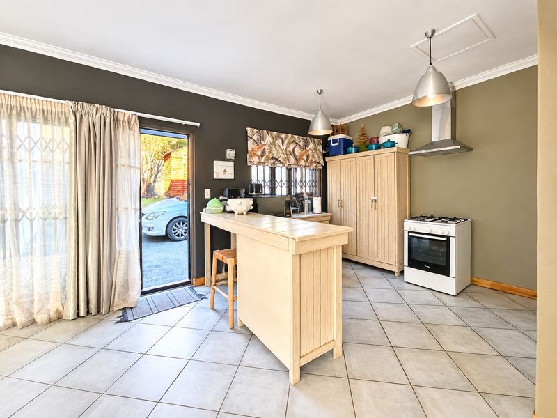Functional kitchen area featuring tiled flooring, a freestanding stove with extractor fan, and direct access to the exterior through a sliding glass door.