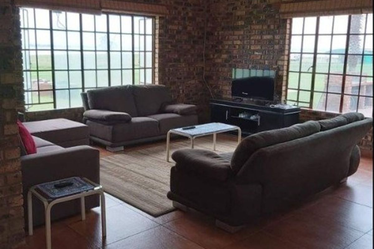 Spacious living room featuring exposed brick walls, large grid-pattern windows, tiled flooring, and a ceiling fan, offering a rustic and comfortable atmosphere.