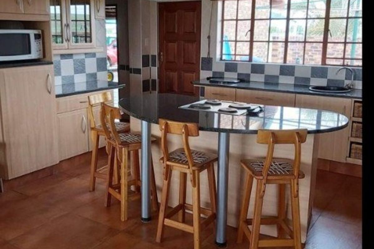 A functional kitchen featuring light wood cabinetry, granite countertops, a central island with a hob, and a distinctive checkered tile backsplash.
