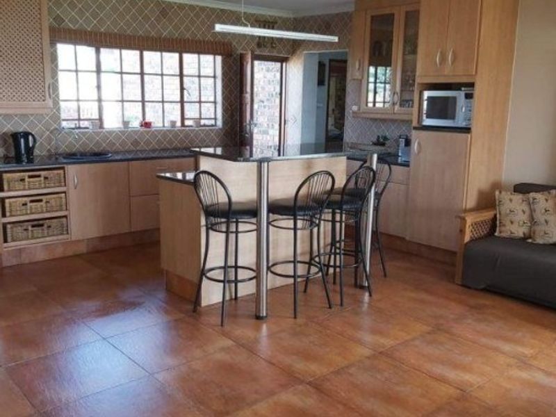 Open-plan kitchen featuring wooden cabinetry, granite countertops, a central island with breakfast bar seating, and tiled flooring throughout.