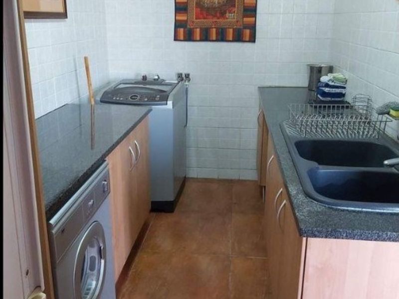 A functional laundry room featuring built-in cabinetry, granite countertops, a double basin sink, and tiled finishes throughout.