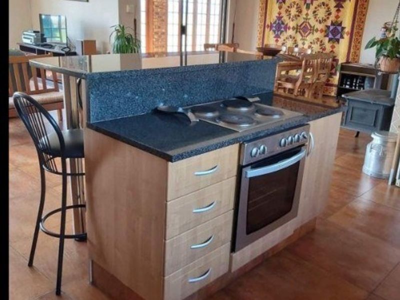 Open-plan living area featuring a central kitchen island with built-in oven, electric cooktop, and granite countertops, leading to a spacious dining and lounge area.
