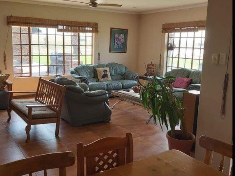 Open plan living area featuring tiled flooring, ceiling fan, and large windows providing natural light and views of the surrounding farm landscape.