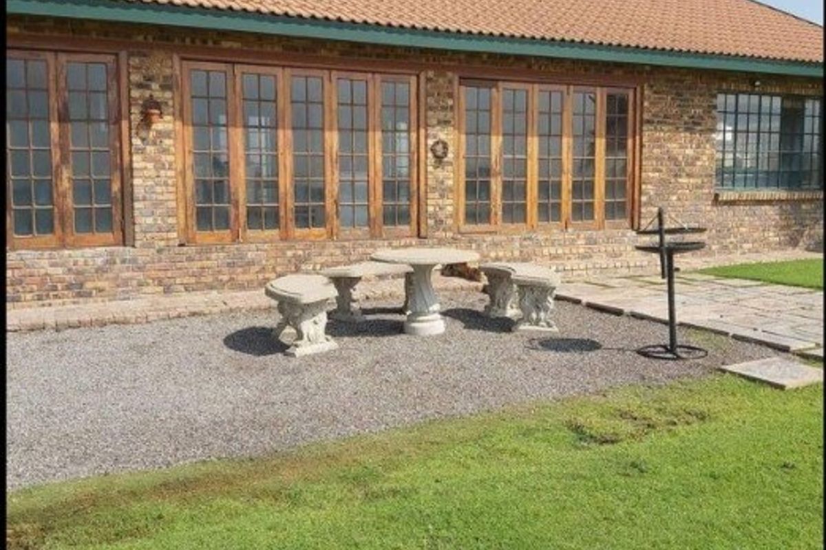 Rear view of a face brick farmhouse featuring extensive timber-framed glass doors opening onto a gravel patio and landscaped lawn.