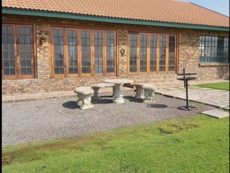 Rear view of a face brick farmhouse featuring extensive timber-framed glass doors opening onto a gravel patio and landscaped lawn.