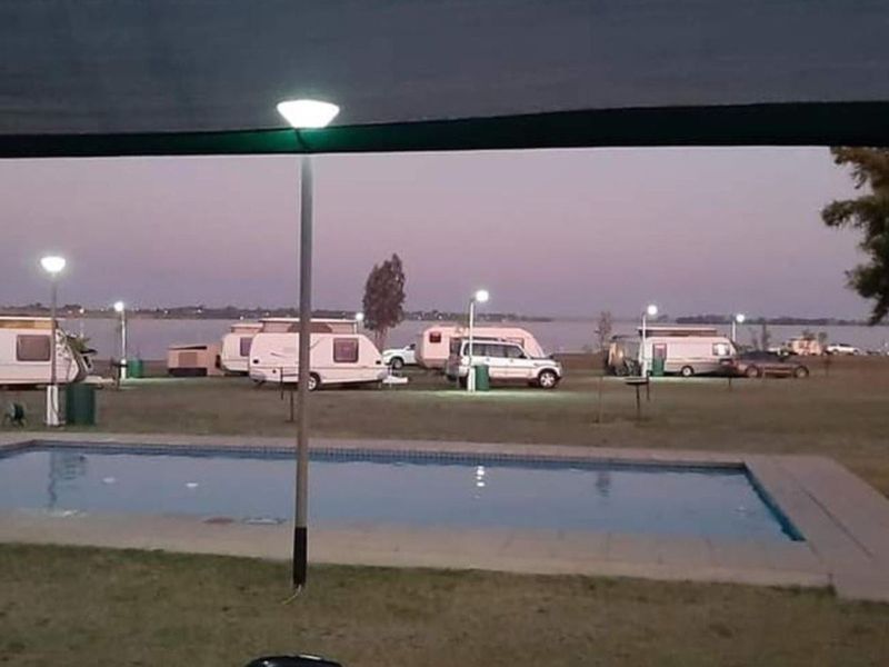 Outdoor pool area overlooking a landscape with caravan park facilities and water views at dusk.
