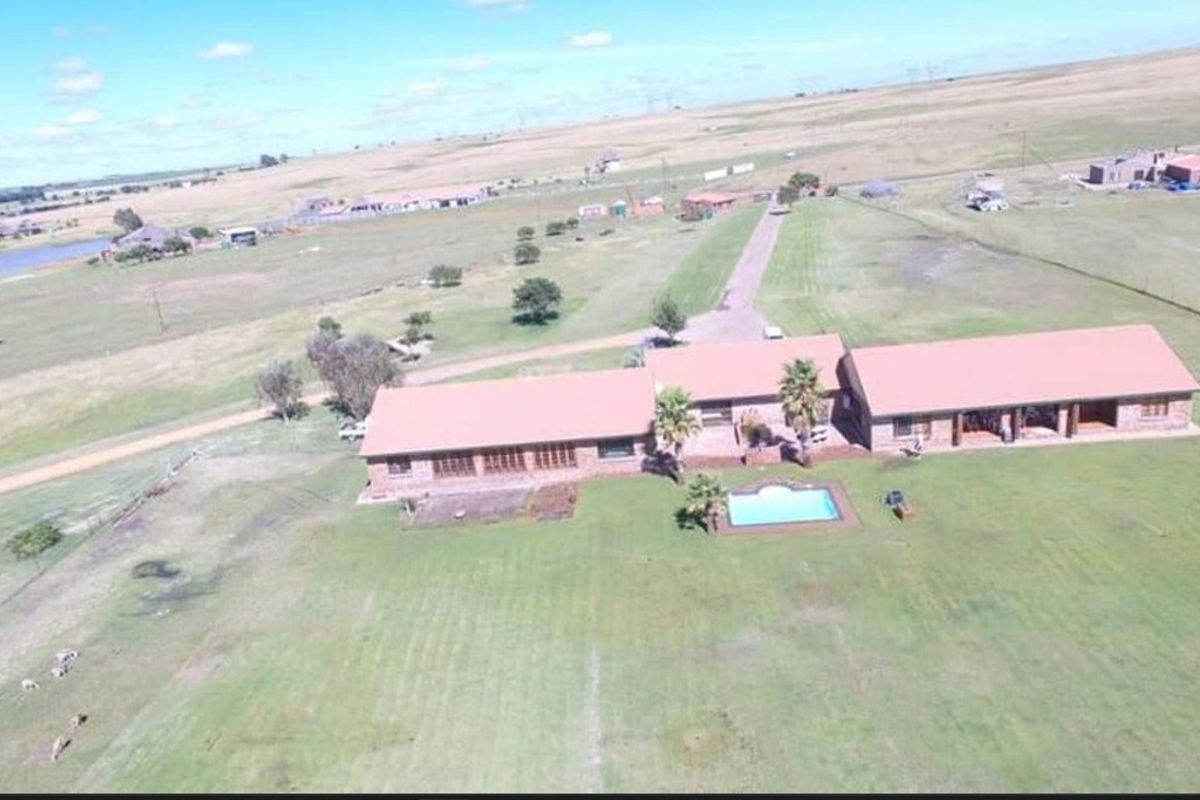 Aerial view of a sprawling farm property featuring a main residence with a swimming pool, expansive grounds, and surrounding rural landscape.