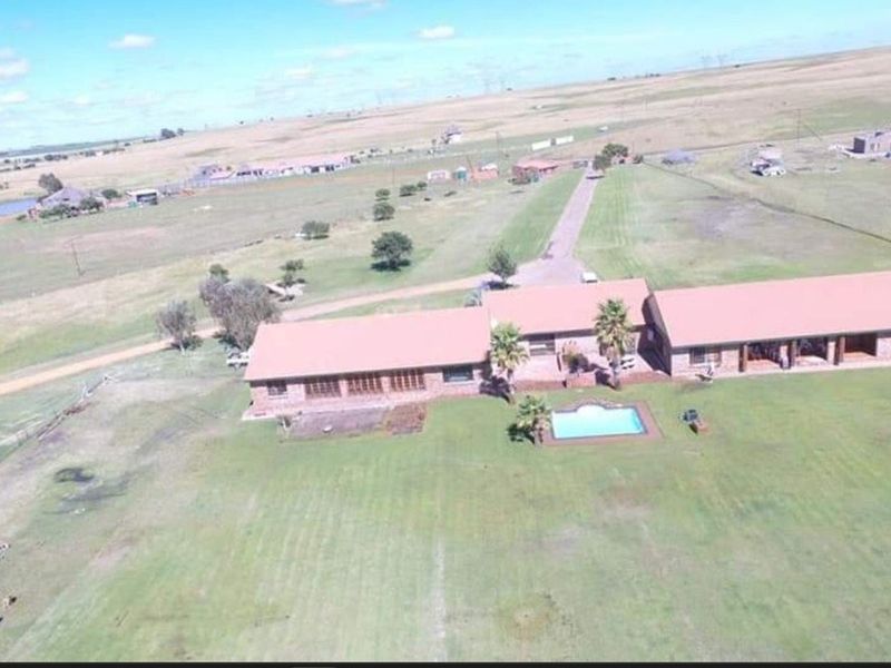 Aerial view of a sprawling farm property featuring a main residence with a swimming pool, expansive grounds, and surrounding rural landscape.