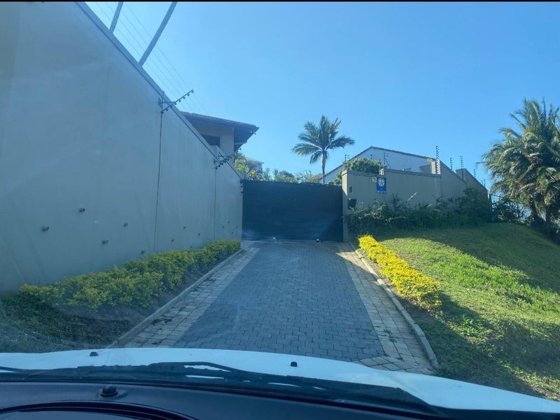 A private paved driveway leading to an automated entrance gate, secured by high perimeter walls with electric fencing.