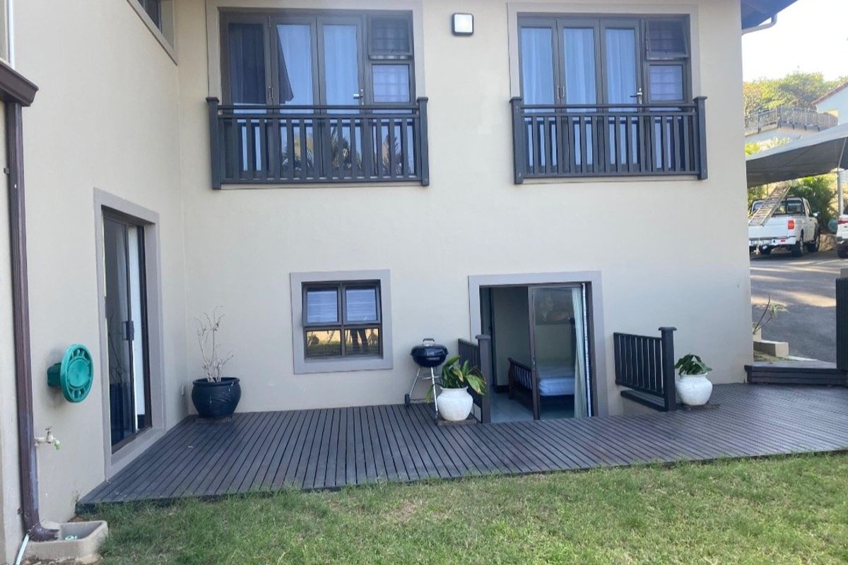 Rear elevation of the house featuring a timber deck, sliding door access to the interior, and upper-level windows with dark-framed balustrades.