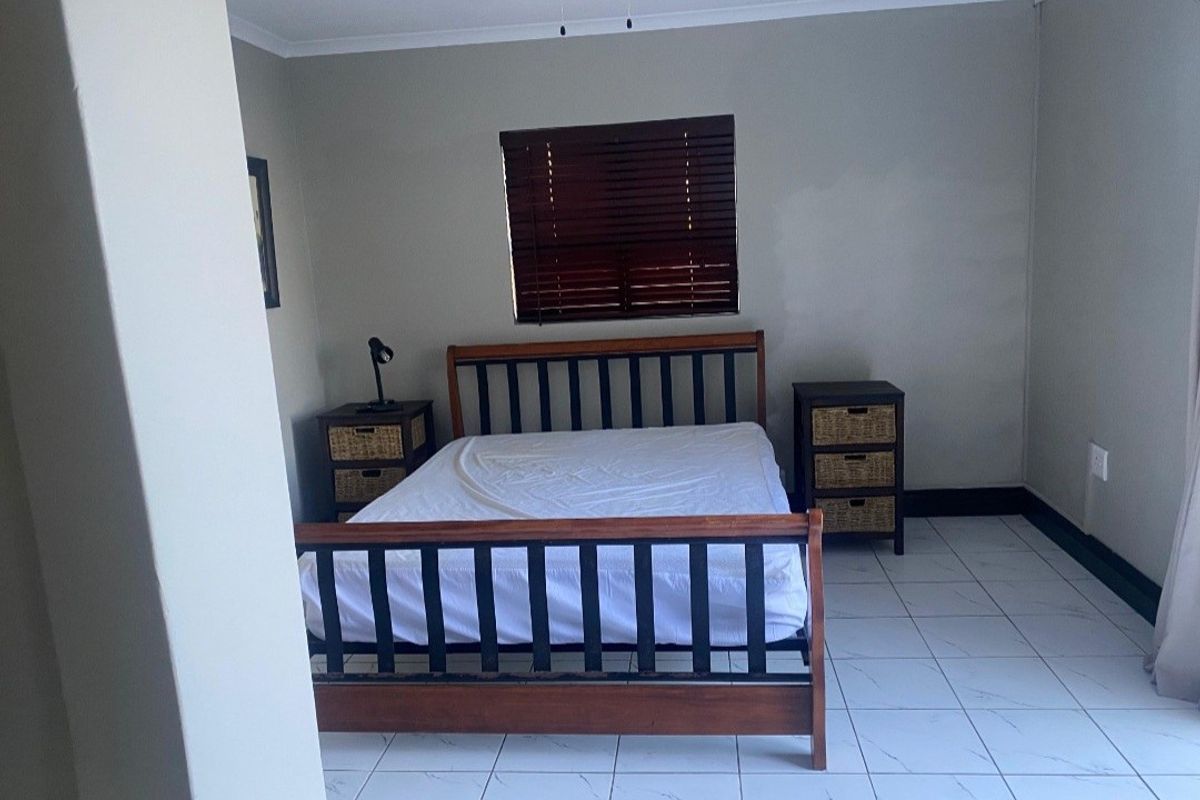 A bedroom featuring tiled flooring, neutral wall paint, and dark wood venetian blinds.