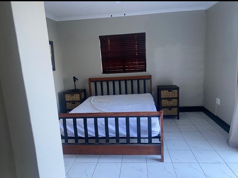 A bedroom featuring tiled flooring, neutral wall paint, and dark wood venetian blinds.