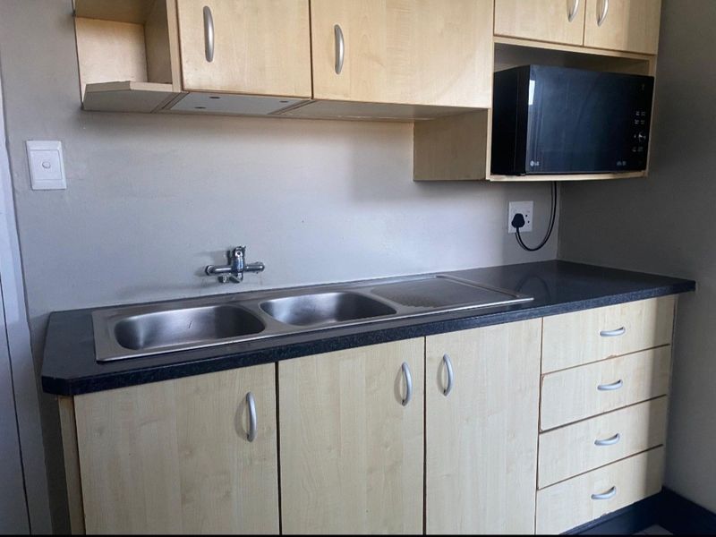 A functional kitchen area featuring light wood-finish cabinetry, a double stainless steel sink, and a dark laminate countertop.