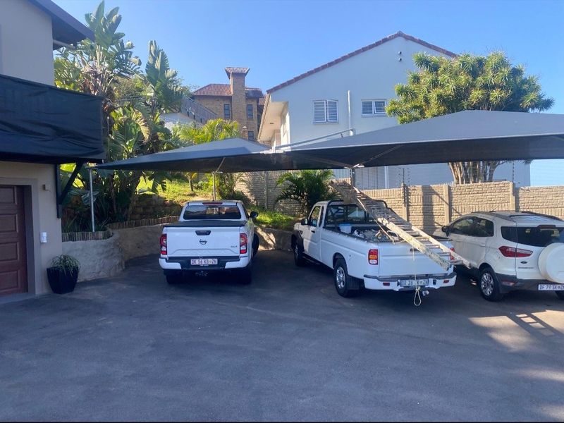 Front exterior view showing a paved driveway with a shade cloth carport structure and perimeter retaining walls.