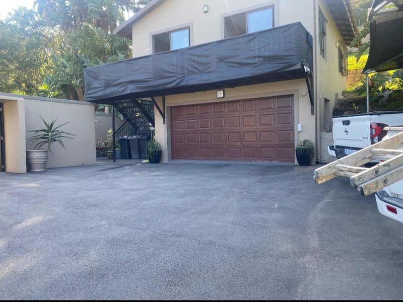 Front exterior view of the property featuring a double garage, an elevated balcony with privacy screening, and an asphalt driveway.