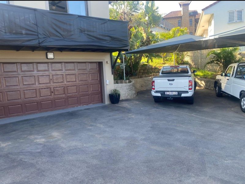 Exterior view of a residential garage with a sectional door, asphalt driveway, and a shade cloth carport structure.