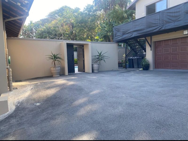 A paved driveway area featuring a garage, external staircase, and a pedestrian gate leading to the rear garden and pool area.
