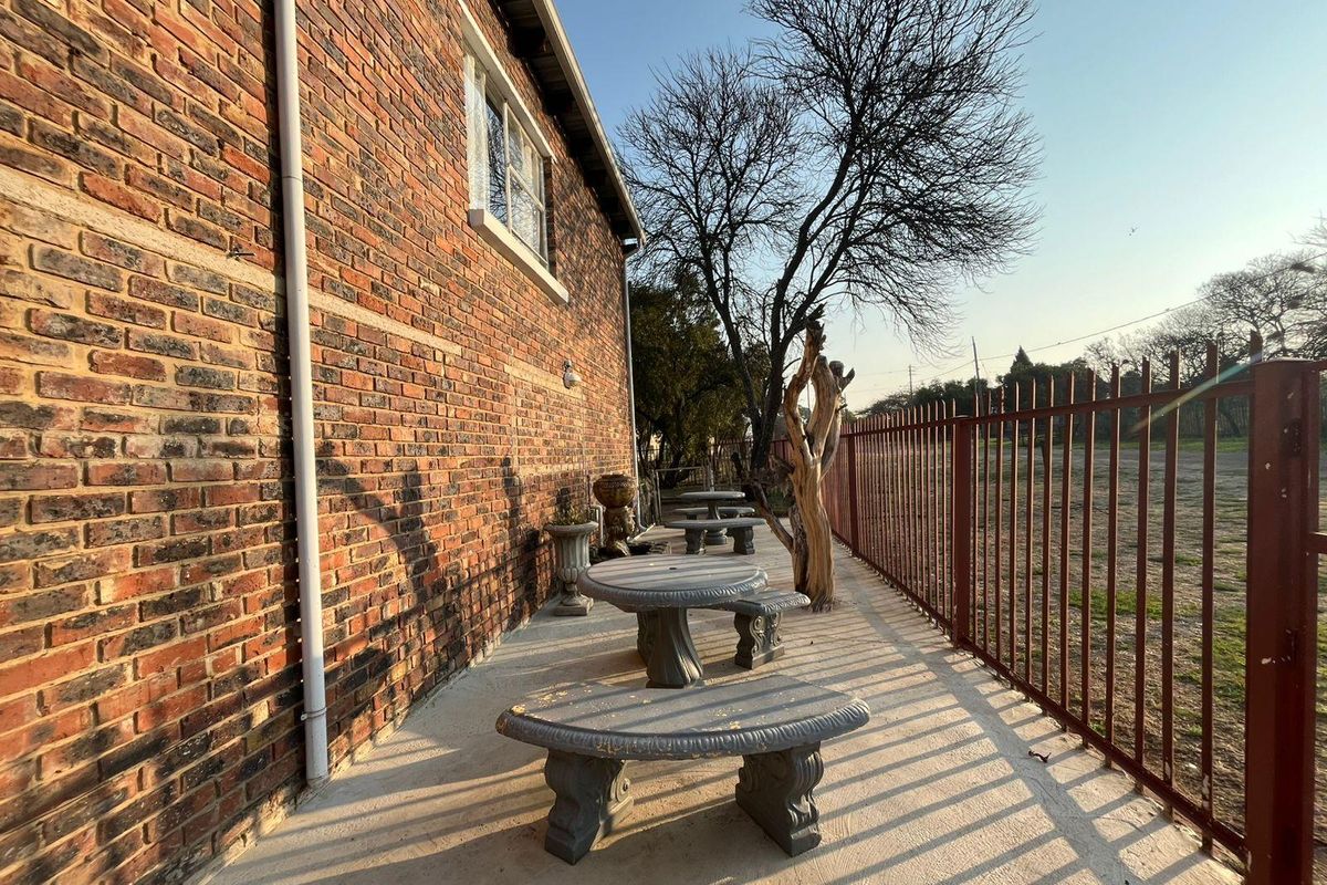 A rear exterior view of the commercial property featuring an exposed brick facade, concrete patio area, and secure metal perimeter fencing.