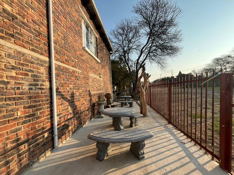 A rear exterior view of the commercial property featuring an exposed brick facade, concrete patio area, and secure metal perimeter fencing.