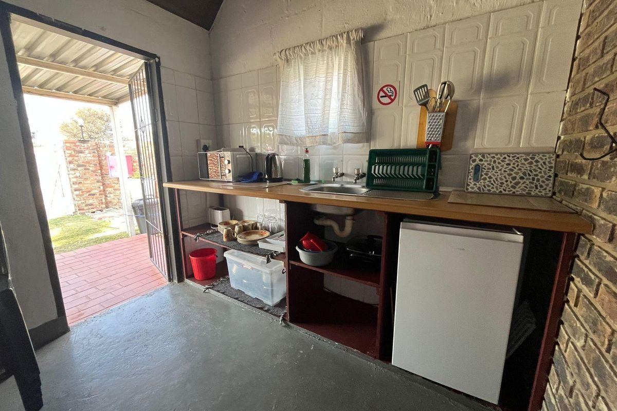 A compact kitchen area featuring a stainless steel sink, tiled splashback, and open shelving, with direct access to an outdoor patio area.