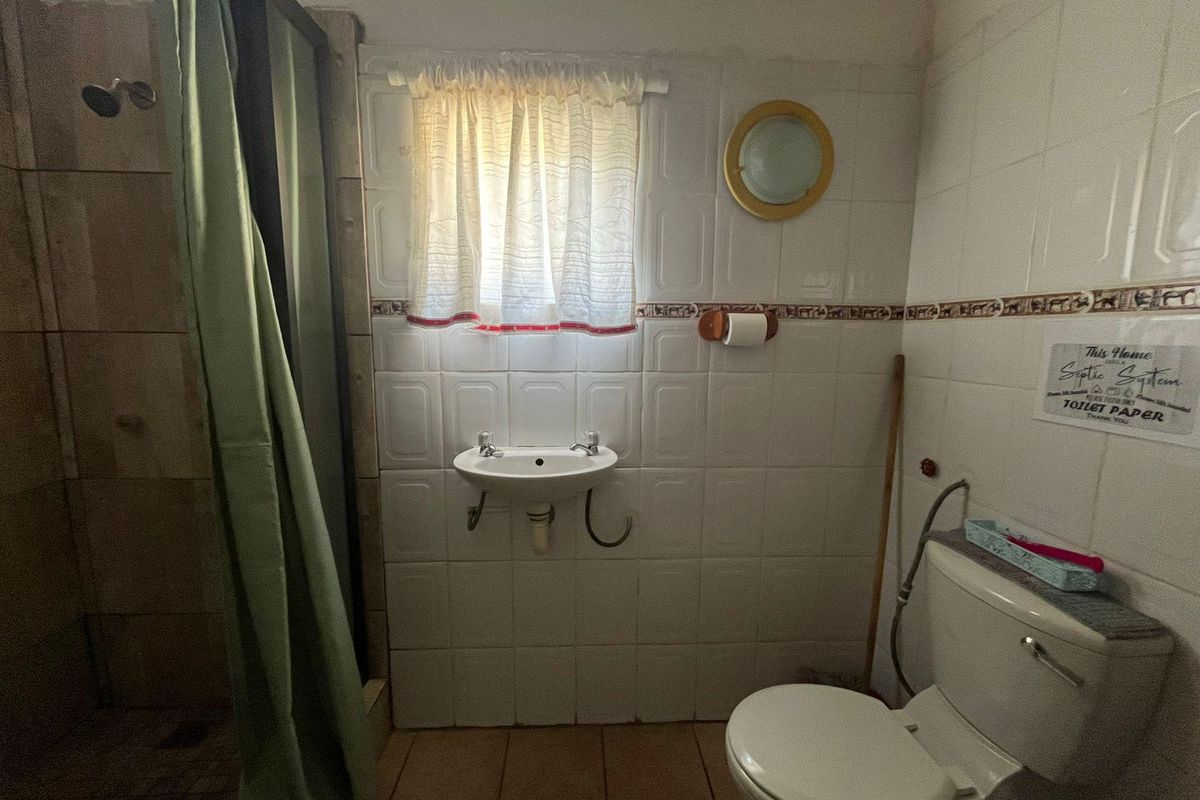 A functional bathroom featuring a wall-mounted basin, shower enclosure, and toilet with tiled walls and flooring, requiring cosmetic updates to improve its overall condition.