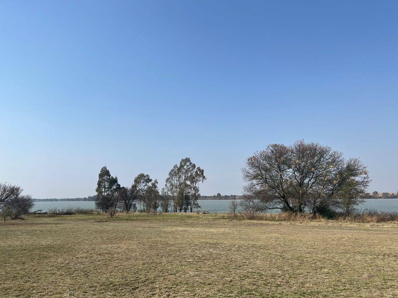 A scenic view of a lakefront property featuring open grassy grounds and mature trees, offering a peaceful natural landscape.
