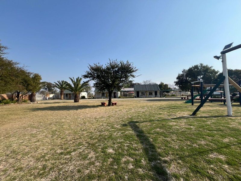 Spacious commercial outdoor grounds featuring landscaped garden areas, mature trees, and multiple building structures with metal roofing.