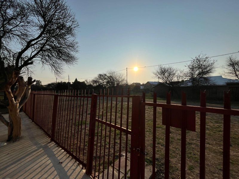 A view of the property frontage featuring metal palisade fencing and a pedestrian gate, overlooking an open grassed area.