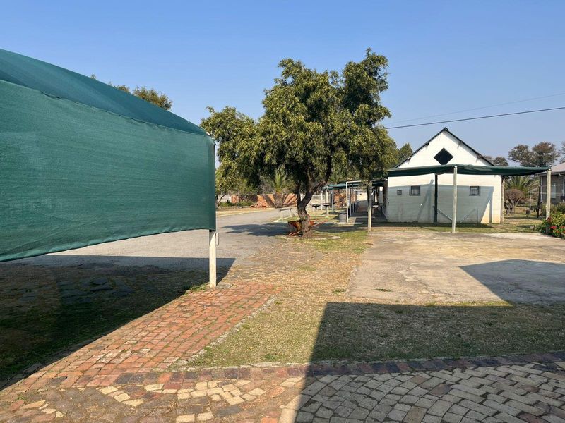 Outdoor commercial area featuring a shade cloth structure, paved driveway, and brick pathways leading to a secondary building structure.