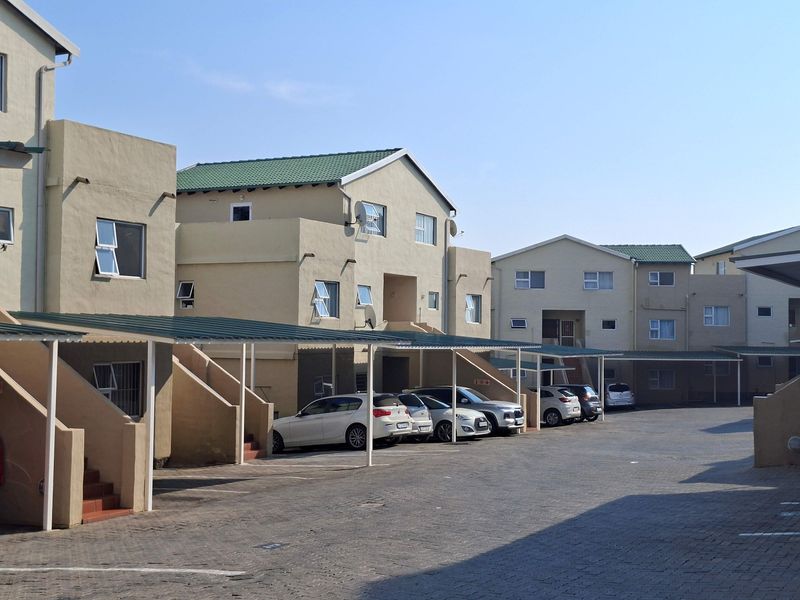 Exterior view of an apartment complex featuring paved parking areas with covered carports and multi-story residential units.