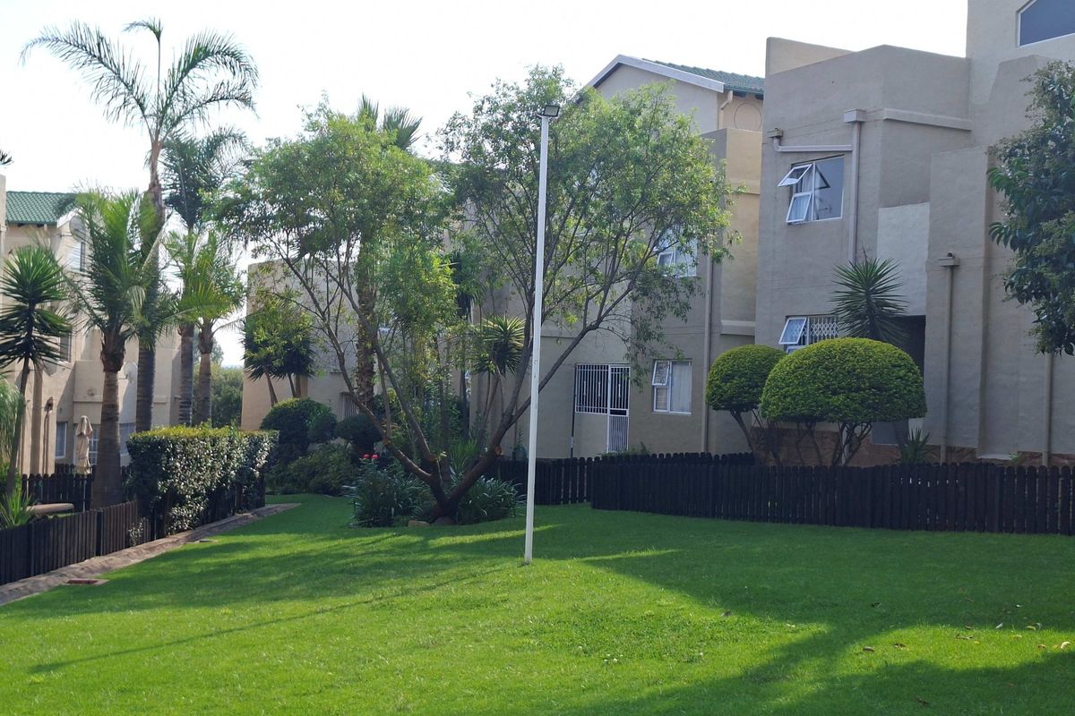 A view of the rear exterior of the apartment complex, featuring well-maintained lawns, mature trees, and secure building access points.