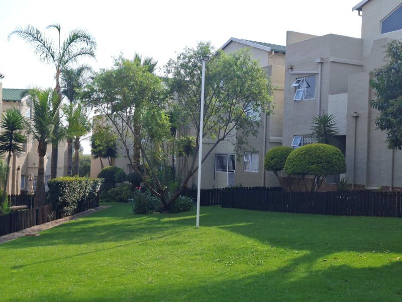 A view of the rear exterior of the apartment complex, featuring well-maintained lawns, mature trees, and secure building access points.