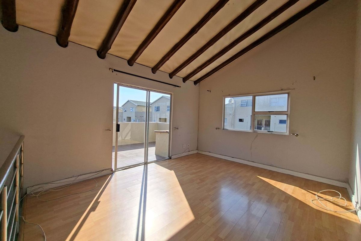 Spacious living area featuring exposed timber ceiling beams, laminate flooring, and direct access to a private balcony through sliding glass doors.