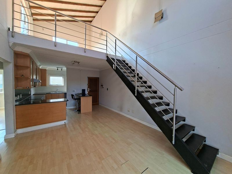 Spacious open-plan living area featuring a modern staircase, mezzanine level, exposed timber beams, and a functional kitchen with granite countertops.